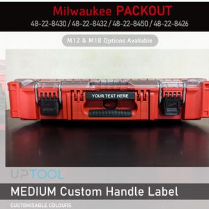 May include: A red Milwaukee PACKOUT toolbox with a clear lid. The box has a black handle with a label that says "YOUR TEXT HERE". The label is customisable. The box is for medium sized tools.