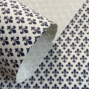 Puede incluir: Papel blanco con un patr&oacute;n repetitivo de flor de lis azul marino. El papel est&aacute; parcialmente enrollado, revelando el interior y la continuidad del patr&oacute;n. Adecuado para envolver, manualidades o fines decorativos.