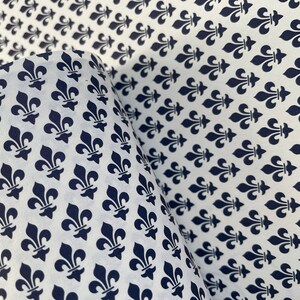 Puede incluir: Papel blanco con un patr&oacute;n repetido de s&iacute;mbolos de flor de lis azul marino. El papel est&aacute; parcialmente enrollado, revelando el patr&oacute;n en el interior. Adecuado para papel de regalo o proyectos de manualidades.