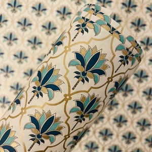 May include: Rolled paper with a repeating floral pattern in teal, navy, and gold on a cream background. The design features stylized lotus flowers and a lattice-like gold outline. The paper is likely for gift wrapping or crafting.