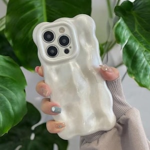 May include: White phone case with a textured, melted-looking design. The case has a raised camera bump with three black camera lenses.