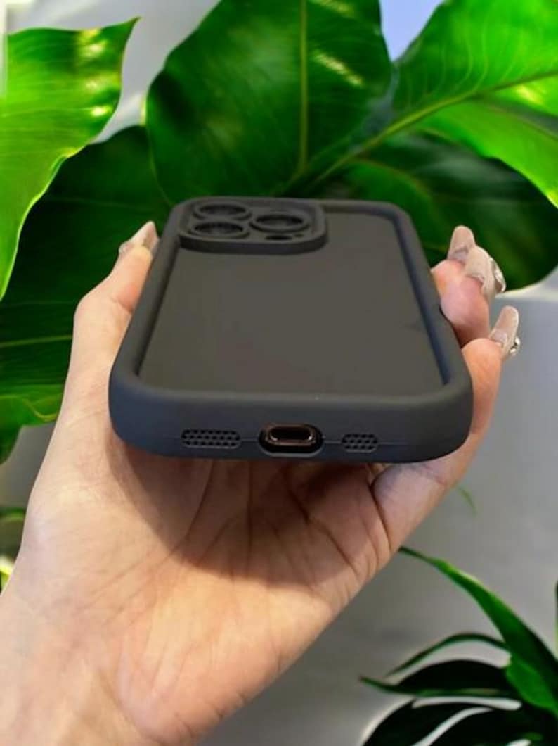 May include: A black silicone phone case with a raised camera lens protector. The case has a smooth, matte finish.