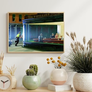 May include: Framed print of Edward Hopper's "Nighthawks" painting. The artwork depicts a diner scene with patrons and a police officer outside. The diner has the word "PHILLIES" on the awning. The print is displayed on a white wall.