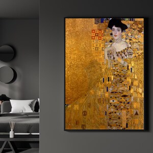May include: A framed art print of a woman in a gold dress, a portrait by Gustav Klimt. The artwork features a woman with a black hat and a detailed gold background. The dress has intricate patterns and details.