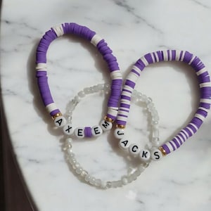 May include: Two purple and white beaded bracelets with the names "AXEEM" and "JACKS" spelled out in white beads.
