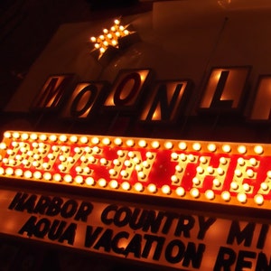 May include: A vintage drive-in movie theater sign with the words "MOONLITE DRIVE-IN THEATRE" in illuminated letters. The sign also includes the text "HARBOR COUNTRY MI AQUA VACATION RENTAL".