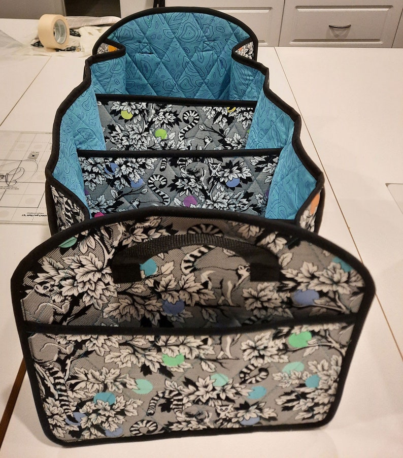 May include: A set of three fabric storage bins with black trim and handles. The bins are lined with a blue quilted fabric and feature a black and white print of leaves and animals.