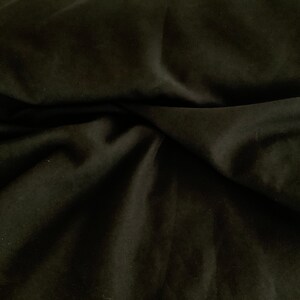 May include: A close-up of a black fabric with a smooth texture. The fabric is folded and draped, creating soft folds and shadows.