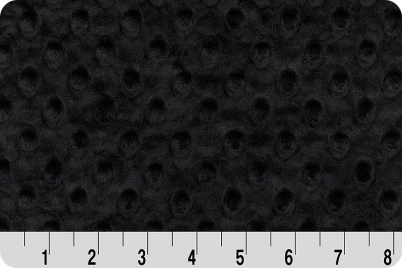 May include: Black minky dot fabric with a subtle texture. The fabric is shown with a ruler for scale.