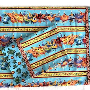 May include: A light blue fabric set featuring a repeating pattern of Native American dancers in colorful attire. The design includes yellow and brown floral stripes and a border with turtles and flowers. The set includes a large rectangle and two smaller pieces.