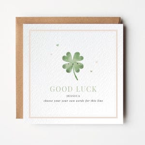 Puede incluir: Tarjeta de felicitación cuadrada con una ilustración de acuarela de un trébol de cuatro hojas con una cara sonriente. La tarjeta dice "GOOD LUCK", el nombre "JESSICA" y una línea para texto personalizado. La tarjeta está en un sobre marrón.