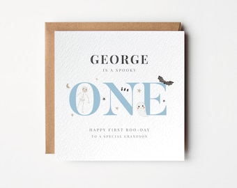 May include: A square card with a brown envelope. The card has the text "GEORGE is a spooky ONE" in dark gray and light blue. The word "ONE" has a skeleton, ghost, and bat illustrations. The card reads "HAPPY FIRST BOO-DAY TO A SPECIAL GRANDSON."