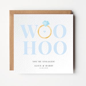 Può includere: Biglietto di annuncio di fidanzamento con sfondo bianco e busta marrone. La carta presenta le parole "WOO HOO" in azzurro, con un anello d'oro e un diamante. È incluso anche il testo "YOU'RE ENGAGED!" e i nomi.