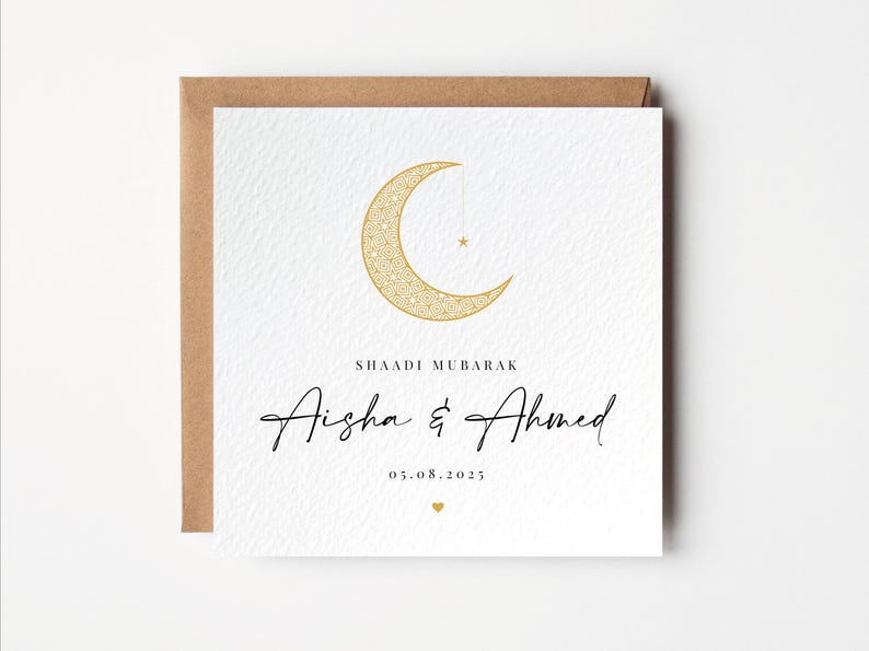 Pu&ograve; includere: Biglietto di nozze bianco con un design a mezzaluna e stella dorate. La carta include il testo "SHAADI MUBARAK" sopra i nomi "Aisha & Ahmed" e la data "05.08.2025". Un piccolo cuore dorato in basso.
