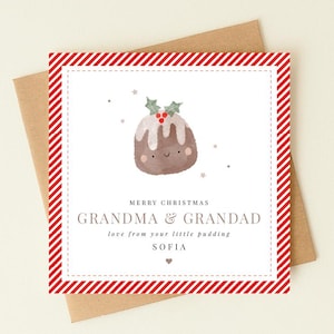 Può includere: Un biglietto d'auguri quadrato con un bordo a strisce diagonali rosse e bianche. Il centro presenta un'illustrazione ad acquerello di un pudding natalizio sorridente con agrifoglio e stelline. Il testo recita: MERRY CHRISTMAS GRANDMA & GRANDAD love from your little pudding SOFIA.