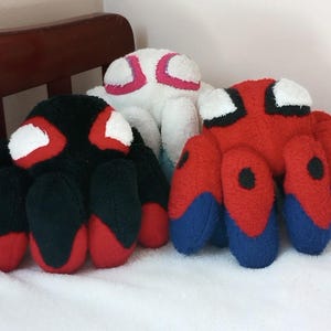 May include: Three plush spider toys. One is black with red accents, one is white with pink accents, and one is red with blue accents.