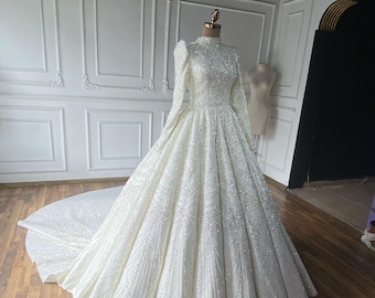 May include: A white wedding dress with long sleeves and a high neckline. The dress is covered in sequins and has a full skirt.