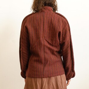 May include: A long-sleeved jacket in a deep rust and dark brown vertical striped pattern. The jacket features a high collar, structured shoulders, and a straight hemline, paired with a solid light brown skirt with a subtle textured finish.