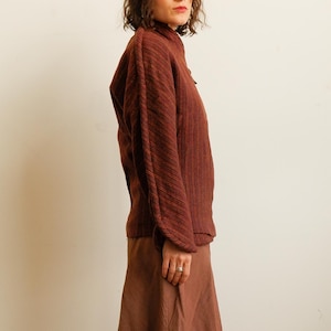 May include: A long-sleeved, dark reddish-brown textured sweater with a high neckline and vertical ribbed detailing, paired with a matching solid brown skirt. The sweater features dropped shoulders and a loose fit, while the skirt has a flared silhouette.