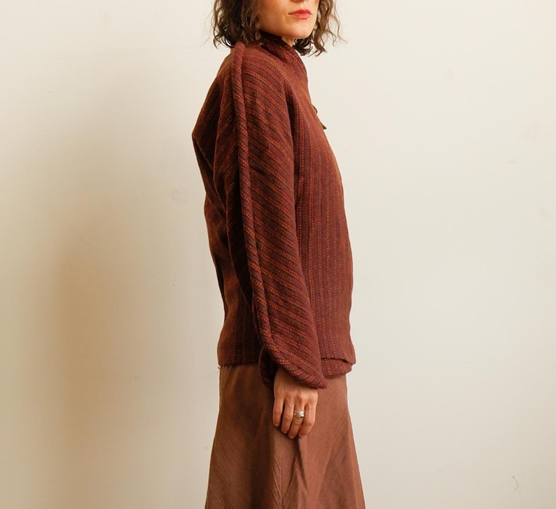 May include: A long-sleeved, dark reddish-brown textured sweater with a high neckline and vertical ribbed detailing, paired with a matching solid brown skirt. The sweater features dropped shoulders and a loose fit, while the skirt has a flared silhouette.