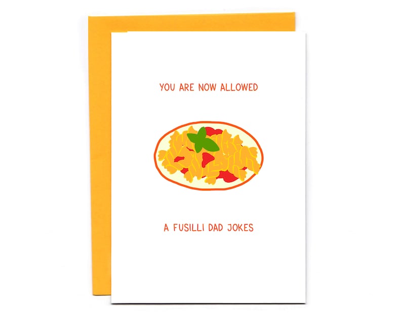 May include: A white card with a yellow border. The card has a cartoon illustration of a plate of fusilli pasta with tomato sauce and a green basil leaf. The text on the card reads "You are now allowed a fusilli dad jokes".