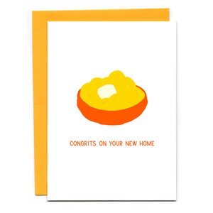 May include: A white card with an orange bowl of yellow grits and a pat of butter. The text "CONGRITS ON YOUR NEW HOME" is printed in black below the bowl.