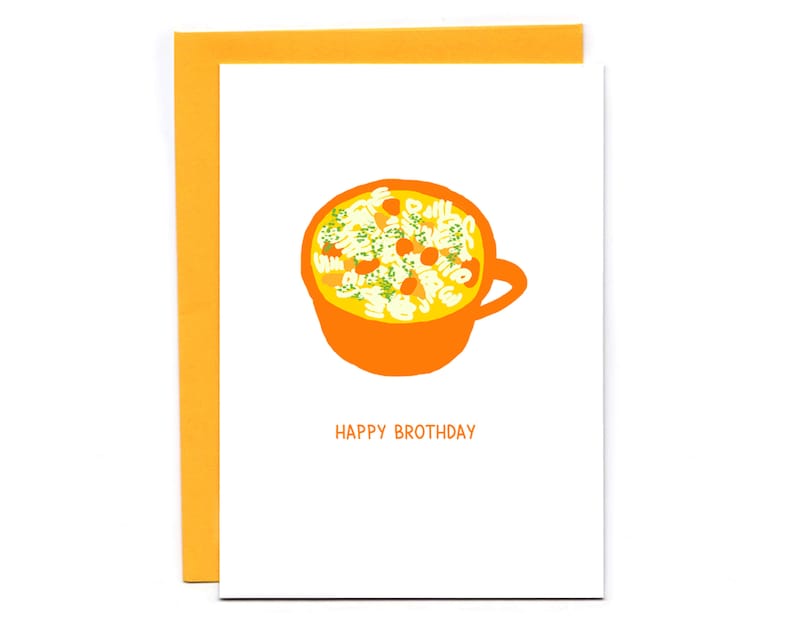 May include: A white card with an orange bowl of yellow noodle soup with green herbs and orange carrots. The text "Happy Brothday" is printed in black below the bowl.