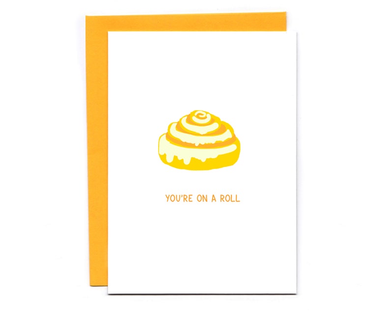 May include: A yellow and white cinnamon roll with the text "You're on a roll" on a white card.