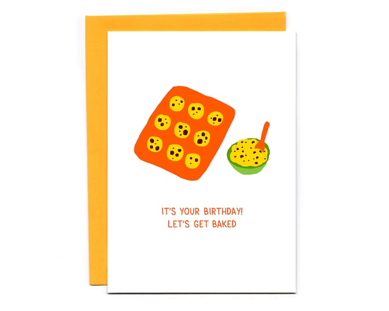 May include: A white card with an orange baking sheet filled with chocolate chip cookies and a green bowl of cookie dough. The text on the card reads "It's your birthday! Let's get baked."