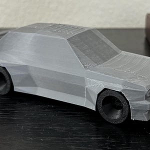 May include: A gray 3D printed model of a car. The model has a detailed exterior with a textured finish.