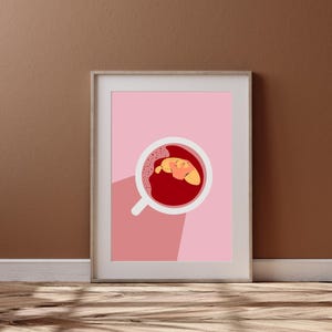 May include: A framed print with a pink background and a white cup with red liquid and a yellow croissant inside. The cup is casting a shadow on the pink background.