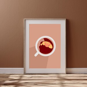 May include: A framed illustration of a white coffee mug with a red liquid and a yellow croissant inside. The background is a light pink colour.
