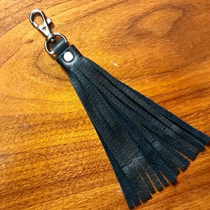 Pode incluir: Um chaveiro de franja de couro preto com um laço de metal prateado.