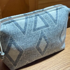 Puede incluir: Un neceser rectangular con un estampado geom&eacute;trico en tonos grises y blancos. La bolsa tiene cierre de cremallera y un peque&ntilde;o lazo con cuentas decorativas. La bolsa est&aacute; hecha de tela texturizada.