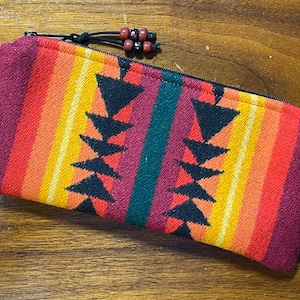 May include: A small zippered pouch with a colorful geometric pattern in shades of red, orange, yellow, green, and black. The pouch has a black zipper and a black cord with red beads.