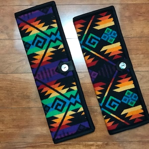 May include: Two black fabric cases with colorful geometric patterns and a button closure. The cases are made of a soft, woven fabric with a black border.