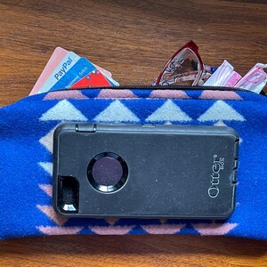 May include: A blue zipped pouch with a geometric pattern, containing a black OtterBox phone case, glasses, and a PayPal business debit card. The pouch is made of a soft, textured material.