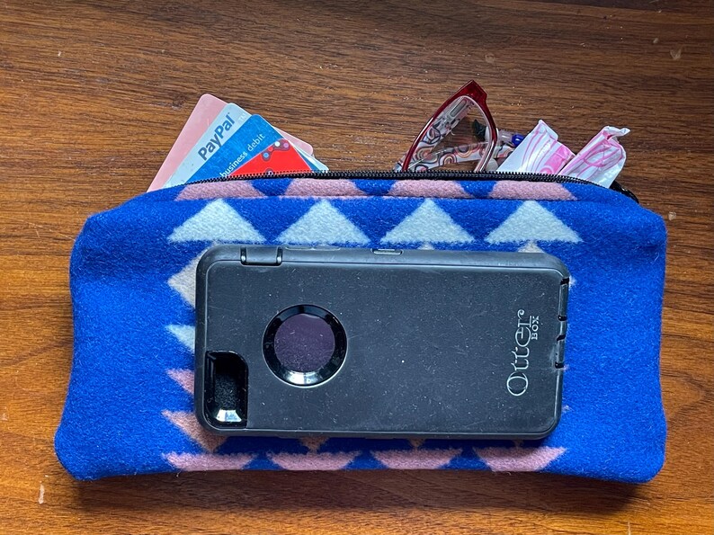 May include: A blue zipped pouch with a geometric pattern, containing a black OtterBox phone case, glasses, and a PayPal business debit card. The pouch is made of a soft, textured material.