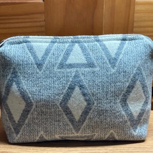 Puede incluir: Peque&ntilde;o neceser rectangular con cierre de cremallera. El neceser es de color azul claro con un patr&oacute;n repetido de diamantes y tri&aacute;ngulos grises. Un peque&ntilde;o tirador con cuentas est&aacute; unido a la cremallera.