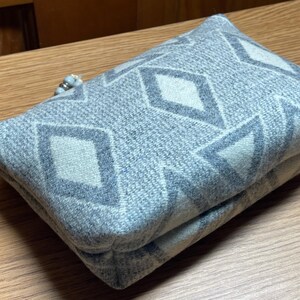 Puede incluir: Un art&iacute;culo de tela rectangular y plegado con un patr&oacute;n geom&eacute;trico de diamantes en tonos grises y blanquecinos. El art&iacute;culo parece ser un embrague o una bolsa peque&ntilde;a, con un detalle de cuentas en un extremo. La tela tiene una apariencia texturizada.