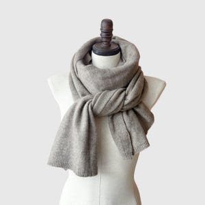 May include: A soft, gray cashmere scarf draped over a mannequin. The scarf is folded and tied in a loose knot at the neck.