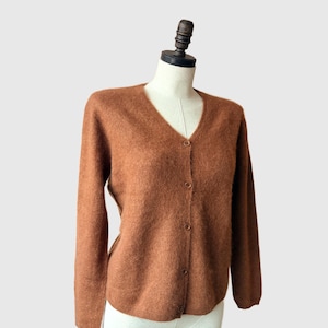 May include: A brown, v-neck cardigan sweater with button closures. The sweater is displayed on a mannequin. The long-sleeved sweater has a soft, textured appearance.