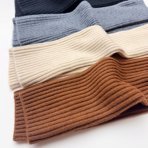 May include: A set of four ribbed knit fabric pieces in a stacked arrangement. The colors from top to bottom are black, slate gray, cream, and warm brown. Each piece features a consistent vertical ribbed texture throughout the entire surface area.