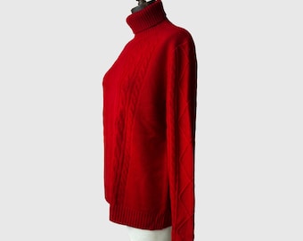 Op de afbeelding: Een rode trui met een rolkraag en een kabelbreipatroon. De trui is op een mannequin en heeft lange mouwen.