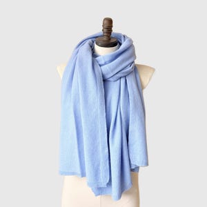 May include: A light blue scarf draped over a mannequin. The scarf is made of a soft material and has a rectangular shape. The scarf is wrapped around the mannequin's neck and shoulders, with the ends hanging down. The scarf is a solid color and appears to be knitted.