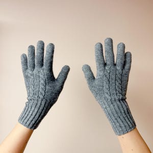 May include: A pair of gray cable knit gloves with a ribbed cuff. The gloves are shown with the fingers extended.