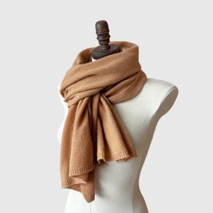 May include: A brown cashmere scarf draped over a white mannequin. The scarf is soft and luxurious, perfect for keeping warm in the winter.