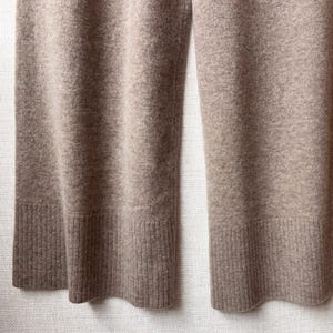 May include: A pair of wide-leg trousers in a light brown colour. The trousers are made of a soft, knitted fabric and have a ribbed cuff at the bottom.