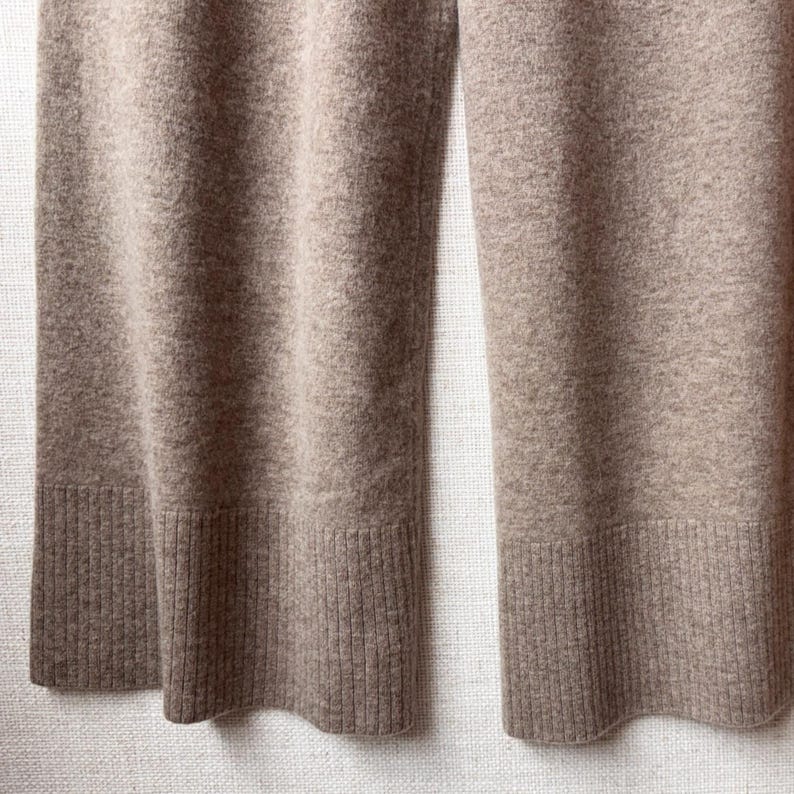 May include: A pair of wide-leg trousers in a light brown colour. The trousers are made of a soft, knitted fabric and have a ribbed cuff at the bottom.