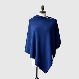 May include: A solid navy blue poncho displayed on a mannequin. The poncho is made of a soft material and has a draped design. The garment is a versatile accessory for cooler weather, offering both style and warmth.